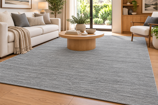 A large gray textured area rug in a modern living room setting with a light wood coffee table, white sofa, and wooden flooring.