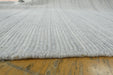 A close-up of a light gray ribbed rug or carpet laid over a wooden floor, showing the texture and edge of the textile.