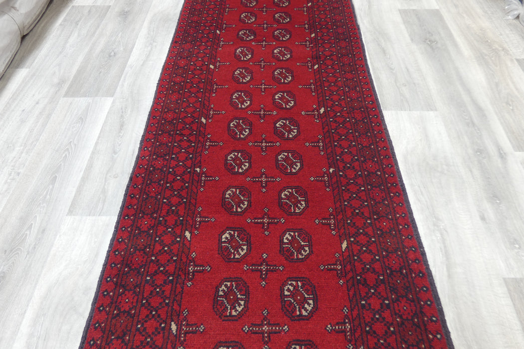 Red Afghan Turkman Bokhara hand-knotted wool hallway runner featuring repeating oval Gul medallions and traditional geometric borders. Rugs Direct NZ