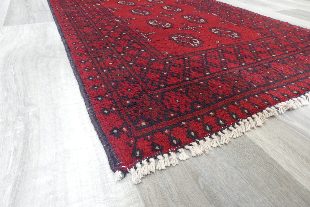 Red Afghan Turkman Bokhara hand-knotted wool hallway runner featuring repeating oval Gul medallions and traditional geometric borders. Rugs Direct NZ