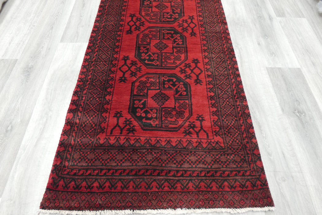 Red Afghan Turkman Bokhara hand-knotted wool hallway runner featuring repeating oval Gul medallions and traditional geometric borders.Rugs Direct NZ