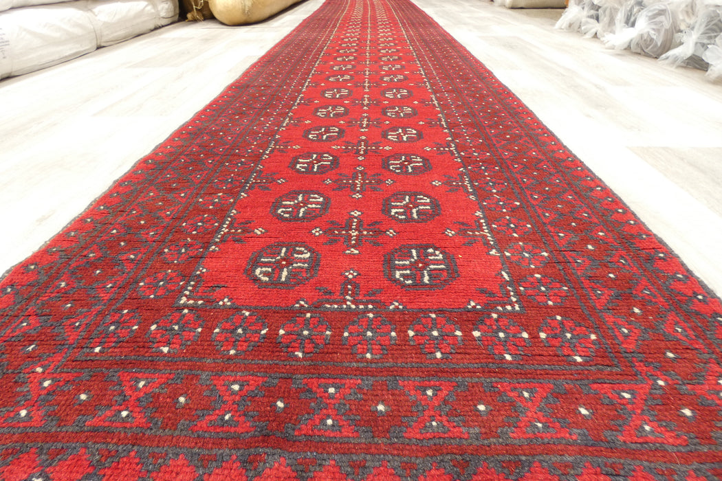 Red Afghan Turkman Bokhara hand-knotted wool hallway runner featuring repeating oval Gul medallions and traditional geometric borders. Rugs Direct NZ