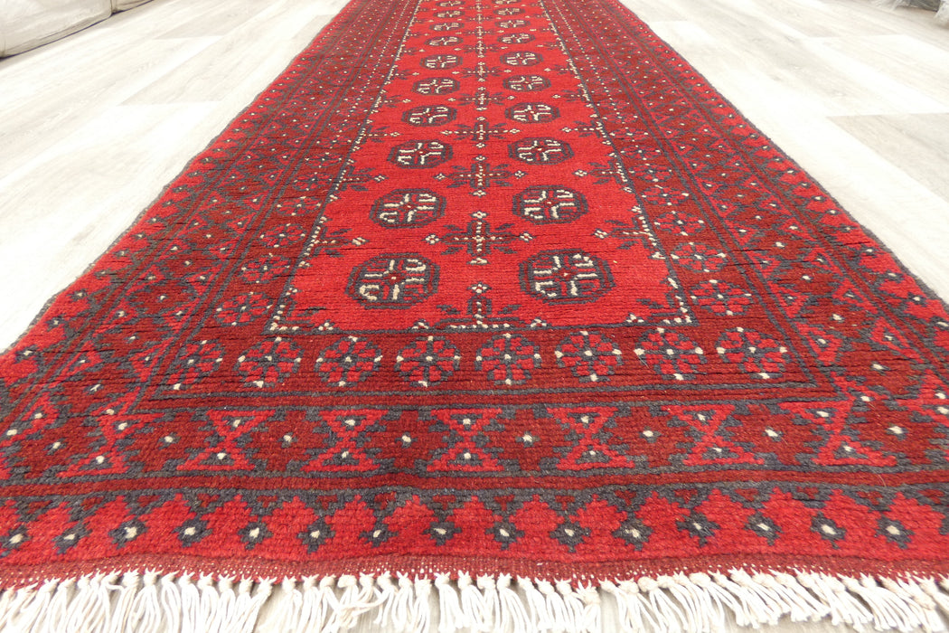 Red Afghan Turkman Bokhara hand-knotted wool hallway runner featuring repeating oval Gul medallions and traditional geometric borders. Rugs Direct NZ