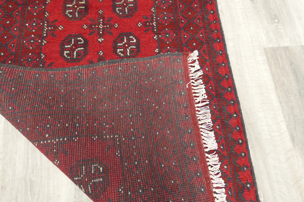 Red Afghan Turkman Bokhara hand-knotted wool hallway runner featuring repeating oval Gul medallions and traditional geometric borders. Rugs Direct NZ