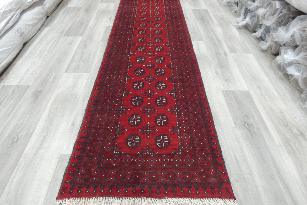 Red Afghan Turkman Bokhara hand-knotted wool hallway runner featuring repeating oval Gul medallions and traditional geometric borders. Rugs Direct NZ